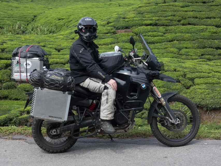 A rider sitting on the loaded BMW GS in front of the tea terraces of the Cameron Highlands.