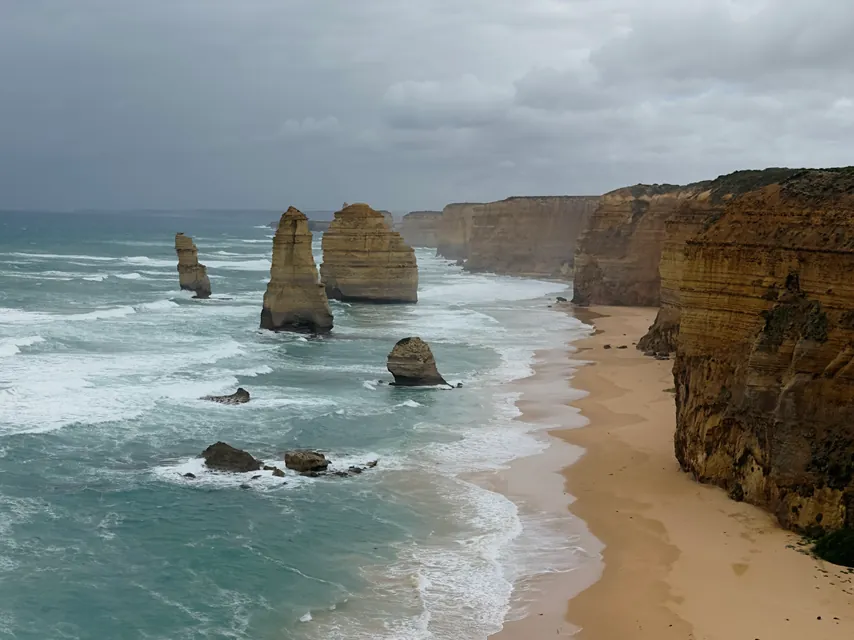 The Twelve Apostles standing off the beach under a grey sky on the Victorian coast.